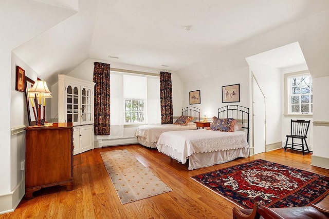 bedroom with vaulted ceiling, hardwood / wood-style floors, and a baseboard heating unit