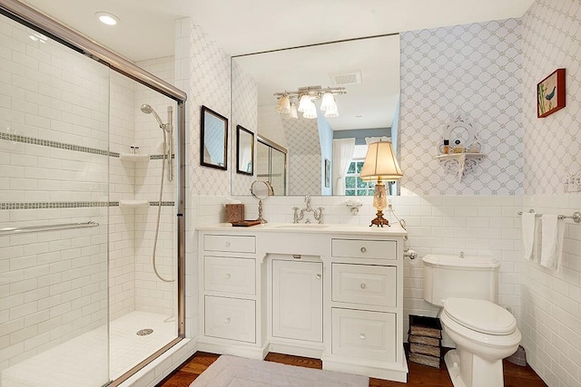 bathroom with a shower with door, vanity, tile walls, and toilet