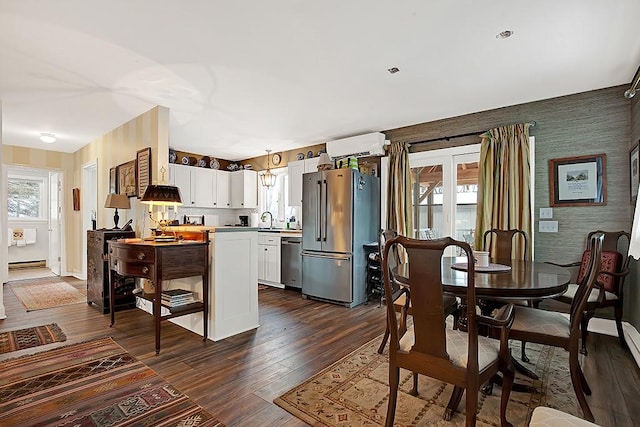 kitchen with a wall unit AC, appliances with stainless steel finishes, dark wood finished floors, white cabinets, and wallpapered walls