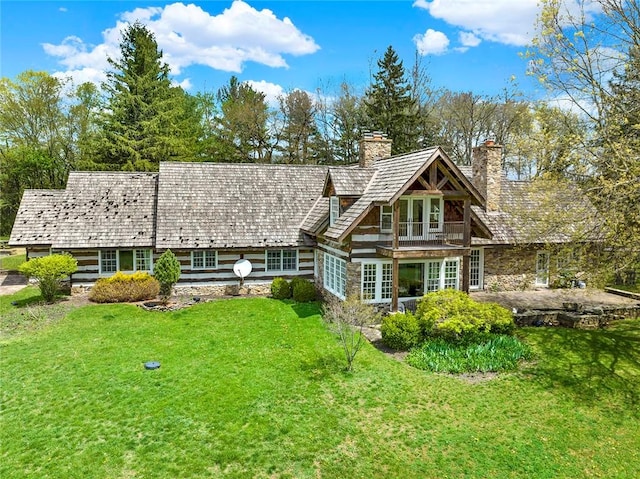 back of property with a chimney, a lawn, a balcony, and stone siding