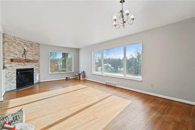 unfurnished living room with wood-type flooring, a stone fireplace, and a notable chandelier