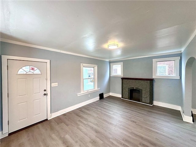 foyer entrance featuring hardwood / wood-style flooring, ornamental molding, and a stone fireplace