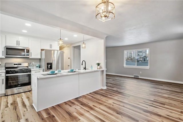 kitchen with pendant lighting, white cabinets, a kitchen island with sink, light hardwood / wood-style floors, and stainless steel appliances