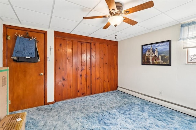 unfurnished bedroom with carpet, a baseboard heating unit, a paneled ceiling, and wooden walls