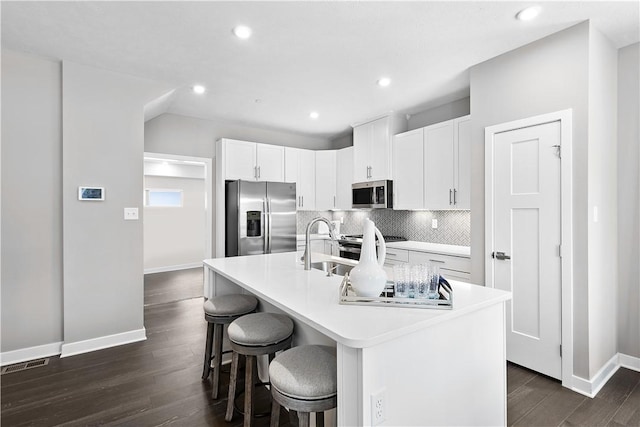 kitchen featuring a breakfast bar area, dark wood-type flooring, appliances with stainless steel finishes, a kitchen island with sink, and white cabinetry