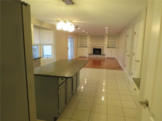 kitchen featuring dark stone countertops, light tile patterned floors, a kitchen island, pendant lighting, and a fireplace