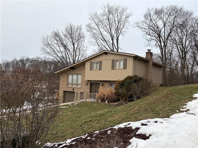 view of front facade featuring a garage, brick siding, a lawn, and a chimney