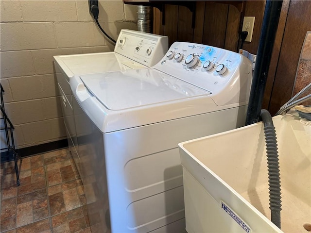 clothes washing area featuring washer and dryer, laundry area, a sink, and concrete block wall