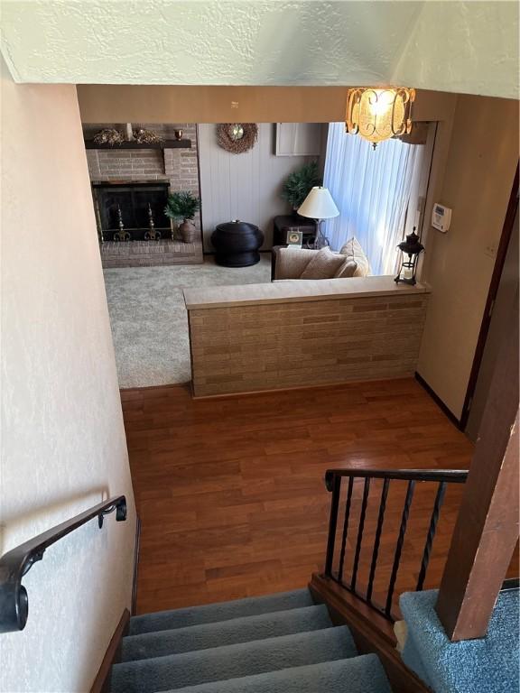 staircase with a brick fireplace, a textured ceiling, and wood finished floors