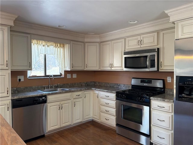 kitchen featuring stainless steel appliances, dark wood-type flooring, a sink, cream cabinetry, and dark countertops