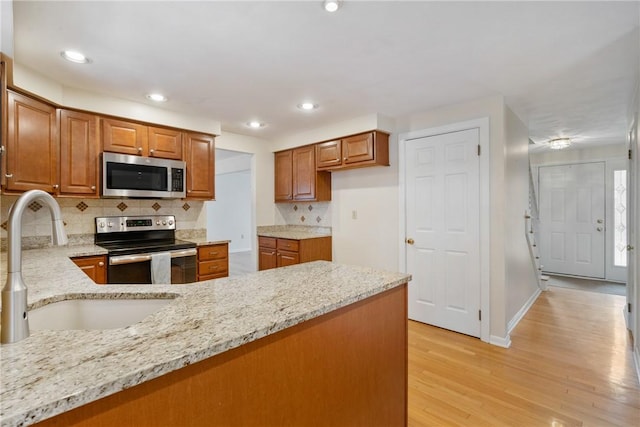 kitchen featuring sink, stainless steel appliances, light stone counters, decorative backsplash, and light wood-type flooring