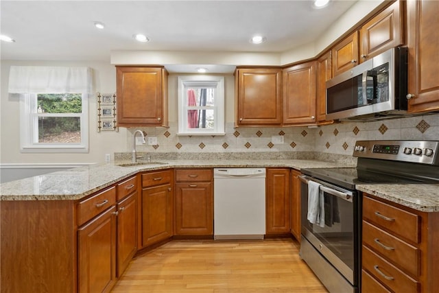 kitchen featuring sink, stainless steel appliances, light stone countertops, kitchen peninsula, and light wood-type flooring