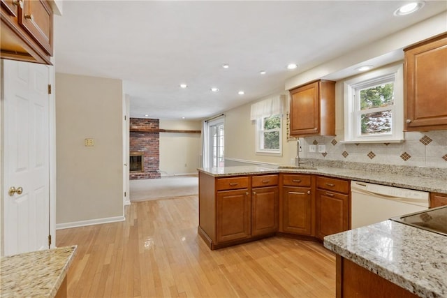 kitchen with light stone counters, a fireplace, kitchen peninsula, and white dishwasher