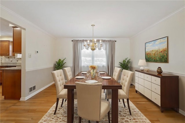 dining area with crown molding, light hardwood / wood-style floors, and a notable chandelier