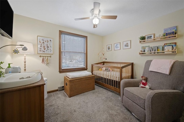 carpeted bedroom featuring sink, a nursery area, ceiling fan, and baseboard heating