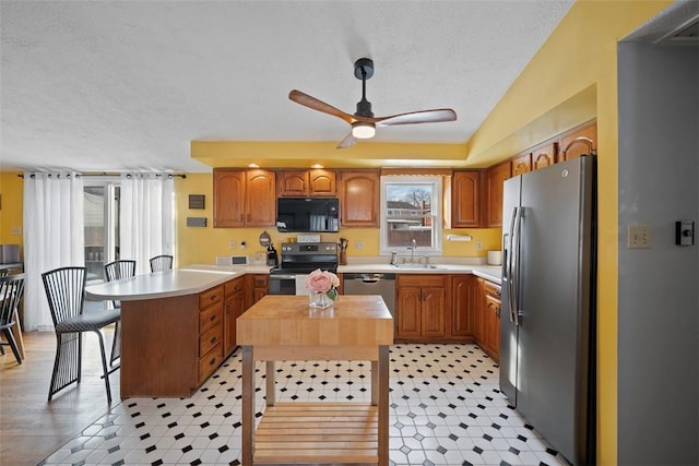 kitchen featuring sink, a center island, a textured ceiling, appliances with stainless steel finishes, and ceiling fan