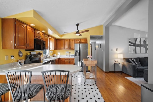 kitchen featuring sink, appliances with stainless steel finishes, vaulted ceiling, kitchen peninsula, and light wood-type flooring