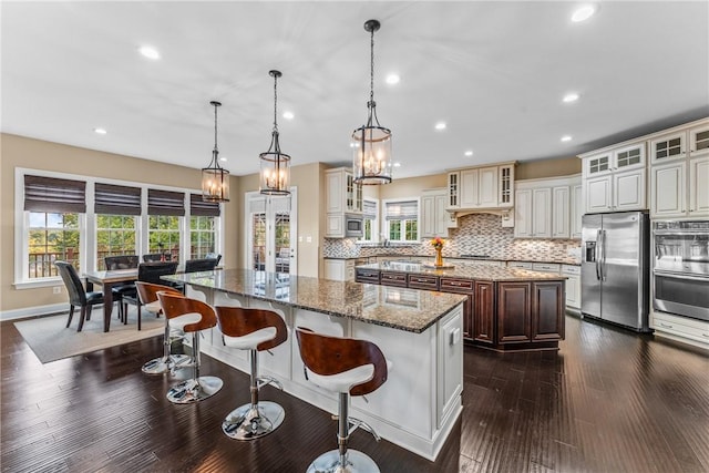 kitchen with a breakfast bar area, hanging light fixtures, stainless steel appliances, a kitchen island, and dark stone counters