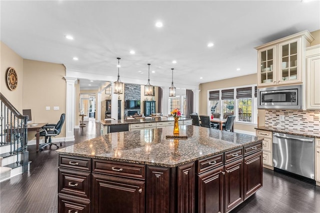 kitchen featuring hanging light fixtures, stainless steel appliances, a center island, cream cabinetry, and ornate columns