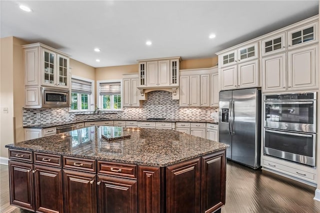 kitchen featuring appliances with stainless steel finishes, dark stone countertops, dark brown cabinetry, tasteful backsplash, and a kitchen island