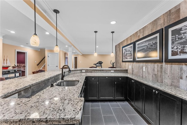 kitchen featuring hanging light fixtures, ornamental molding, sink, and light stone counters