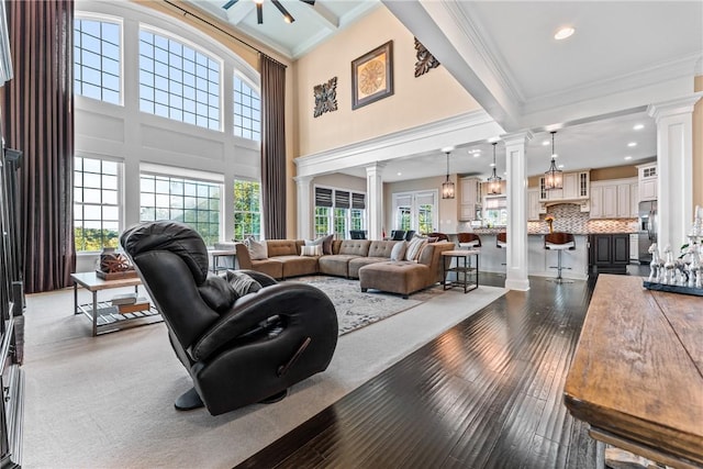 living room featuring ornate columns, a towering ceiling, wood-type flooring, ornamental molding, and ceiling fan