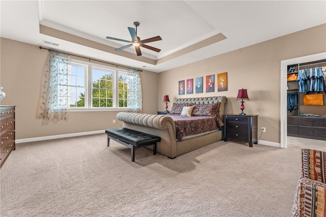 carpeted bedroom with ceiling fan, a walk in closet, ornamental molding, and a tray ceiling