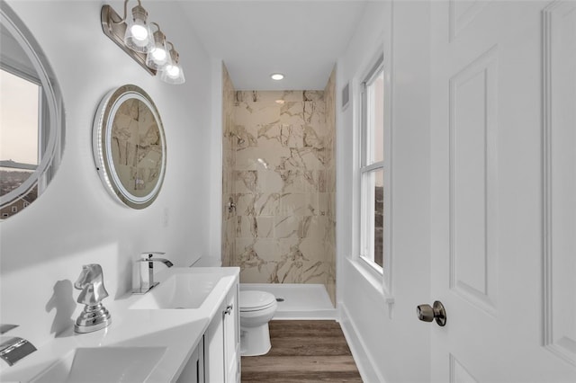 bathroom with a tile shower, vanity, wood-type flooring, and toilet