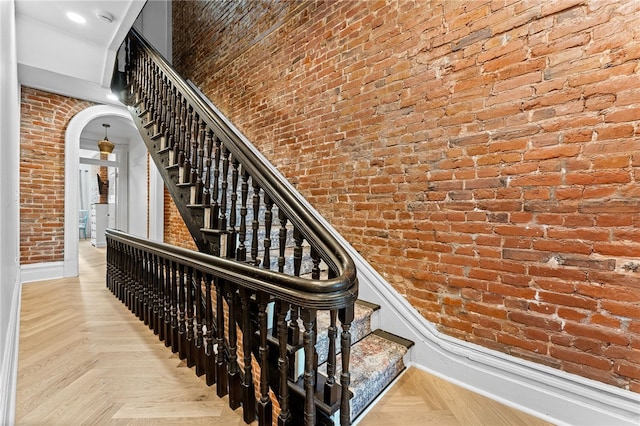 staircase featuring brick wall, parquet flooring, and a towering ceiling