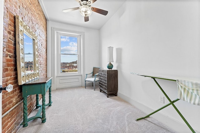 living area with brick wall, light colored carpet, and ceiling fan