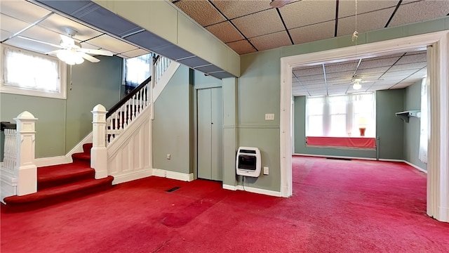 basement featuring a paneled ceiling, carpet flooring, heating unit, and ceiling fan