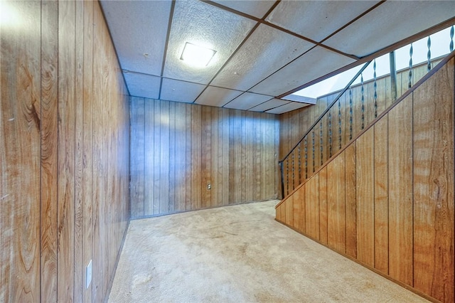 basement with a paneled ceiling, wooden walls, and carpet floors