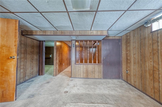 carpeted empty room with wooden walls and a drop ceiling