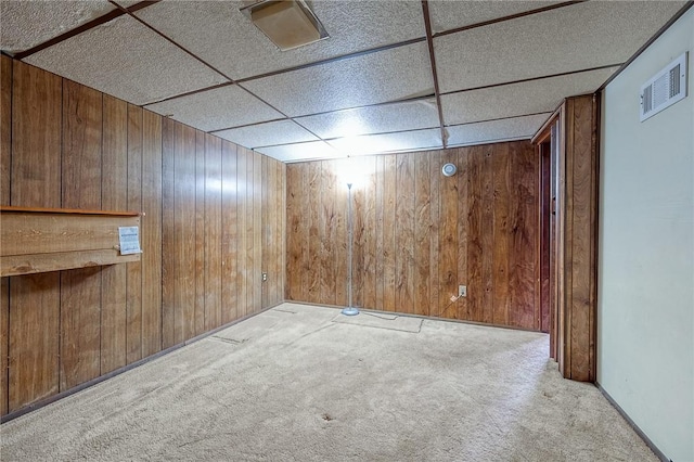 carpeted spare room featuring a drop ceiling and wood walls