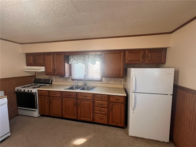 kitchen with white appliances, a sink, under cabinet range hood, wainscoting, and ornamental molding