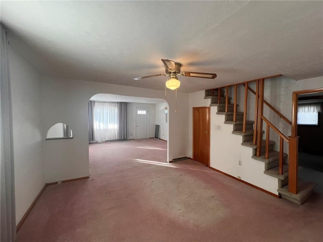 unfurnished living room featuring arched walkways, a ceiling fan, carpet, and stairway