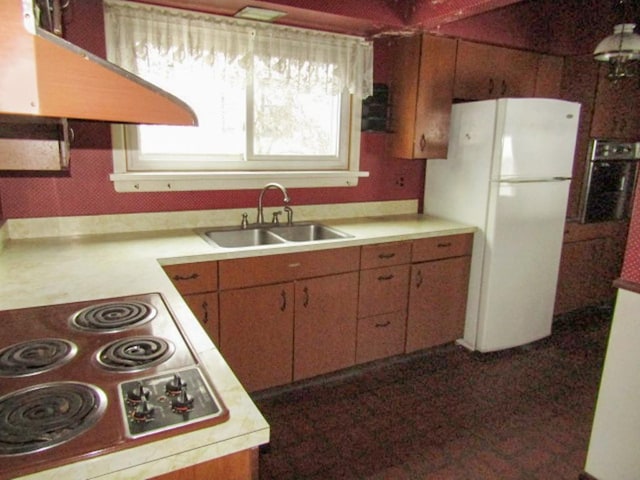 kitchen with wall chimney exhaust hood, cooktop, sink, stainless steel oven, and white fridge