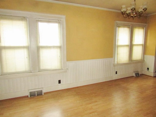 unfurnished room featuring ornamental molding, an inviting chandelier, and light wood-type flooring