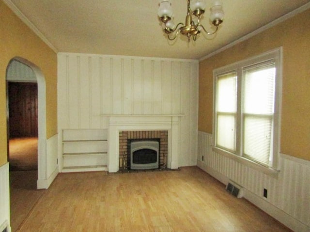 unfurnished living room with crown molding, a fireplace, a chandelier, and hardwood / wood-style flooring