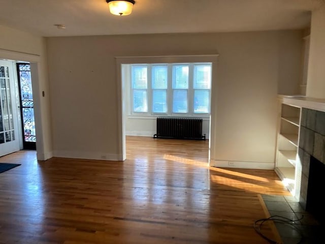 unfurnished living room with wood-type flooring, radiator, and a tile fireplace