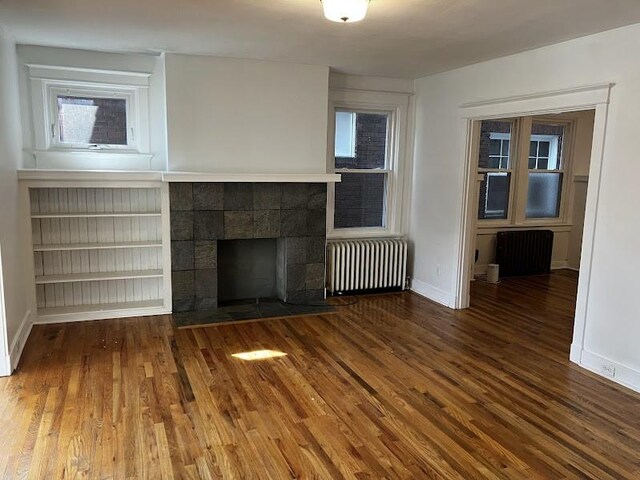 unfurnished living room featuring a tiled fireplace, hardwood / wood-style flooring, and radiator heating unit