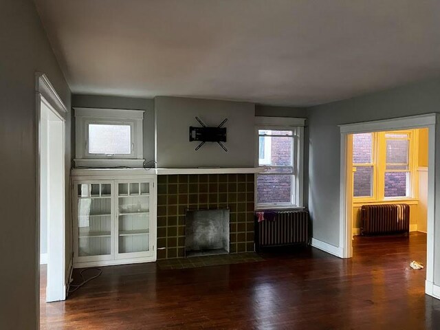 unfurnished living room with dark wood-type flooring, radiator heating unit, and a tile fireplace