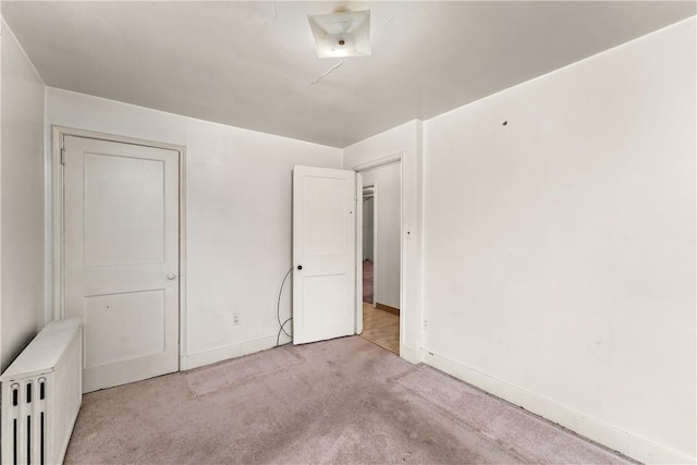 unfurnished bedroom featuring light carpet and radiator heating unit