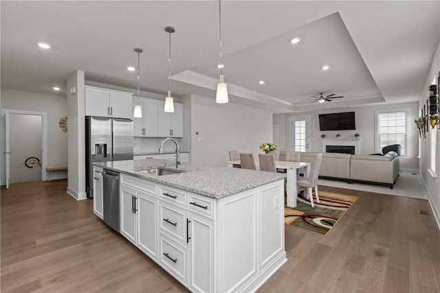 kitchen featuring a kitchen island with sink, sink, white cabinets, and a tray ceiling