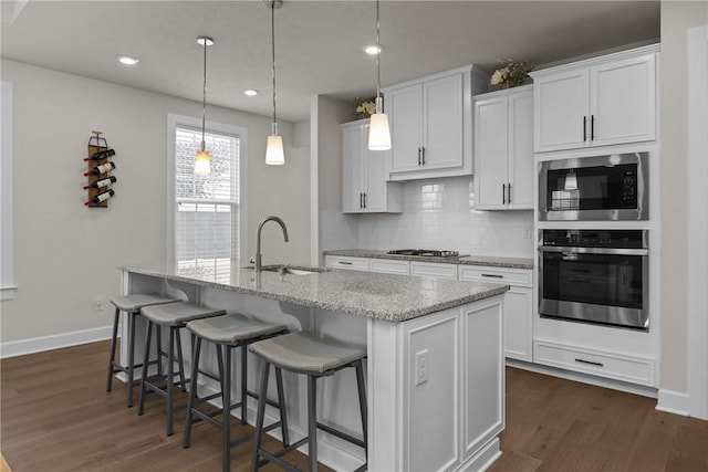 kitchen featuring appliances with stainless steel finishes, pendant lighting, white cabinetry, sink, and a center island with sink