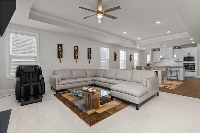 carpeted living room featuring a raised ceiling, crown molding, and ceiling fan