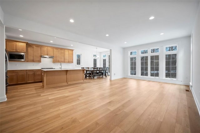 kitchen featuring sink, hanging light fixtures, light hardwood / wood-style flooring, stainless steel microwave, and a kitchen island