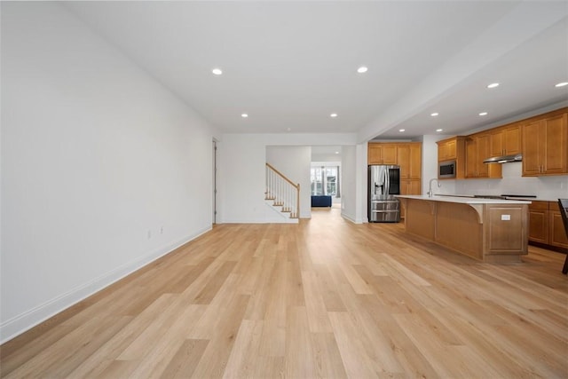 kitchen with a kitchen bar, sink, light hardwood / wood-style flooring, appliances with stainless steel finishes, and an island with sink