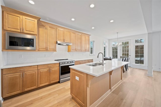 kitchen with built in microwave, an island with sink, sink, stainless steel range with electric cooktop, and hanging light fixtures