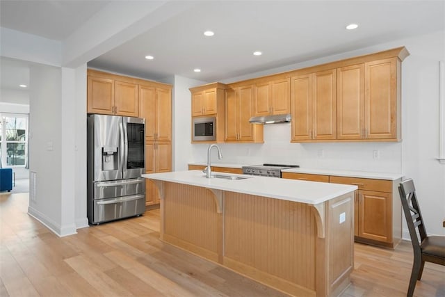 kitchen featuring sink, a breakfast bar area, appliances with stainless steel finishes, light hardwood / wood-style floors, and an island with sink